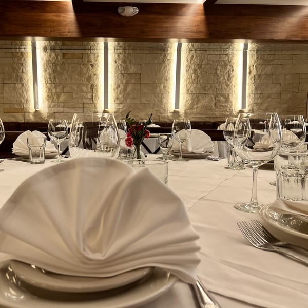 Elegantly set dining table with white tablecloths, wine glasses, and folded napkins at Alba's Pizzeria.