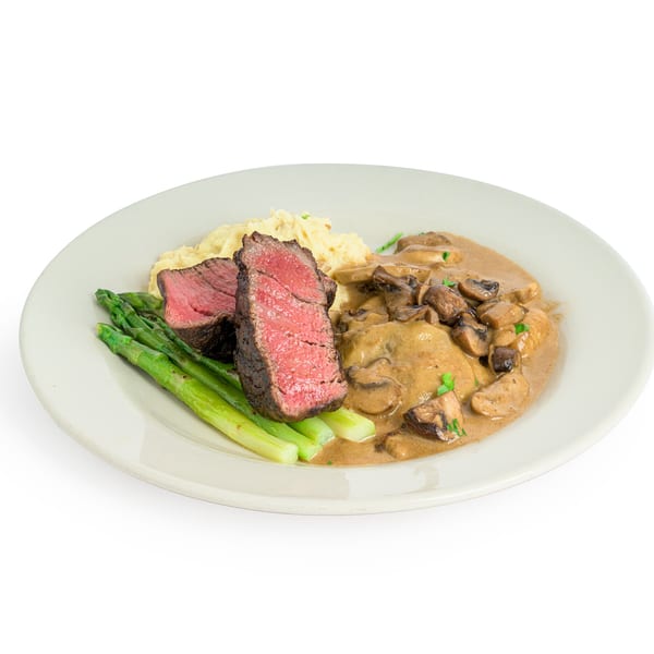 Steak with mashed potatoes, asparagus, and a mushroom cream sauce on a white plate.