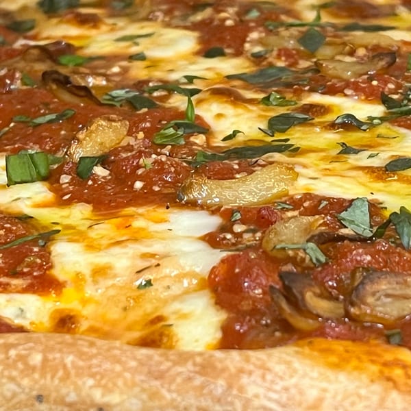 Close-up of a hot Alba's Pizzeria pizza with melted cheese, red sauce, garlic, and basil.