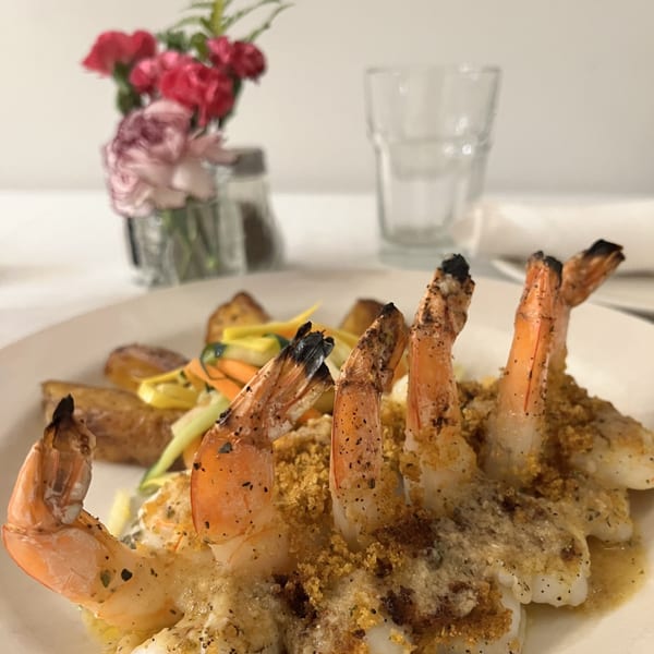 Garlic shrimp with vegetables on a white plate, with flowers and a glass in the background.