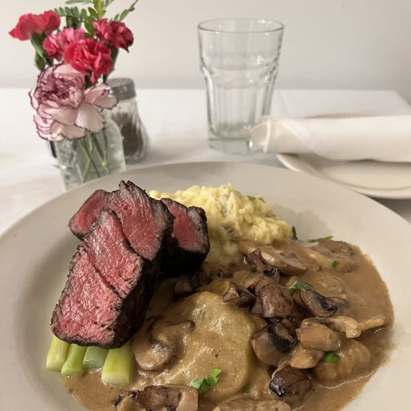 Steak with mashed potatoes, gnocchi in mushroom sauce, and asparagus, with flowers and a glass.
