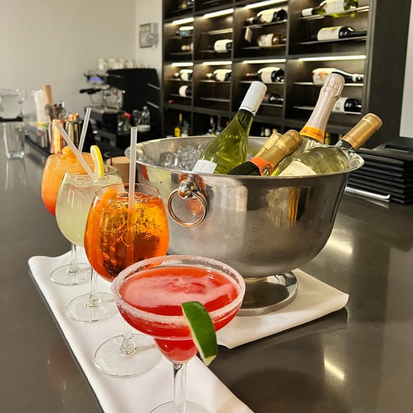 Colorful cocktails and a wine bucket with bottles on a bar at Alba's Pizzeria & Restaurant.