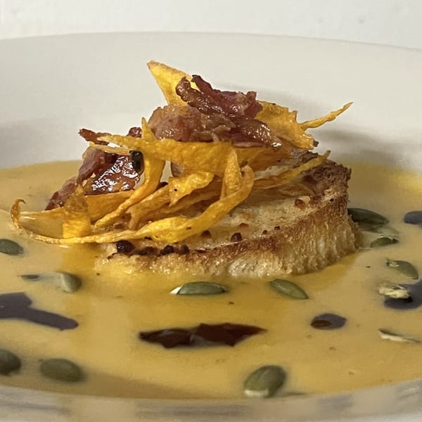 Creamy orange soup with a crouton, crispy fried onions, bacon bits, and pumpkin seeds.
